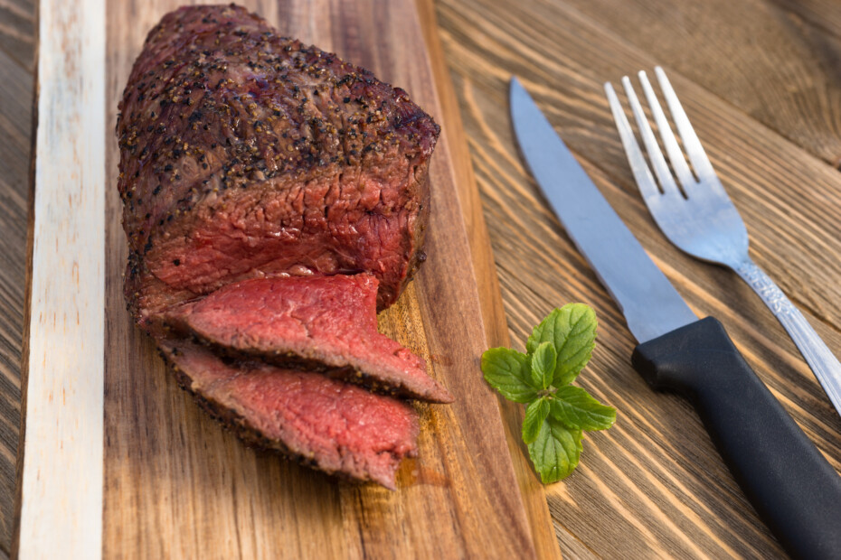 A Large Piece Of Grilled Top Sirloin Sits On Cutting Board Sliced And Peppered