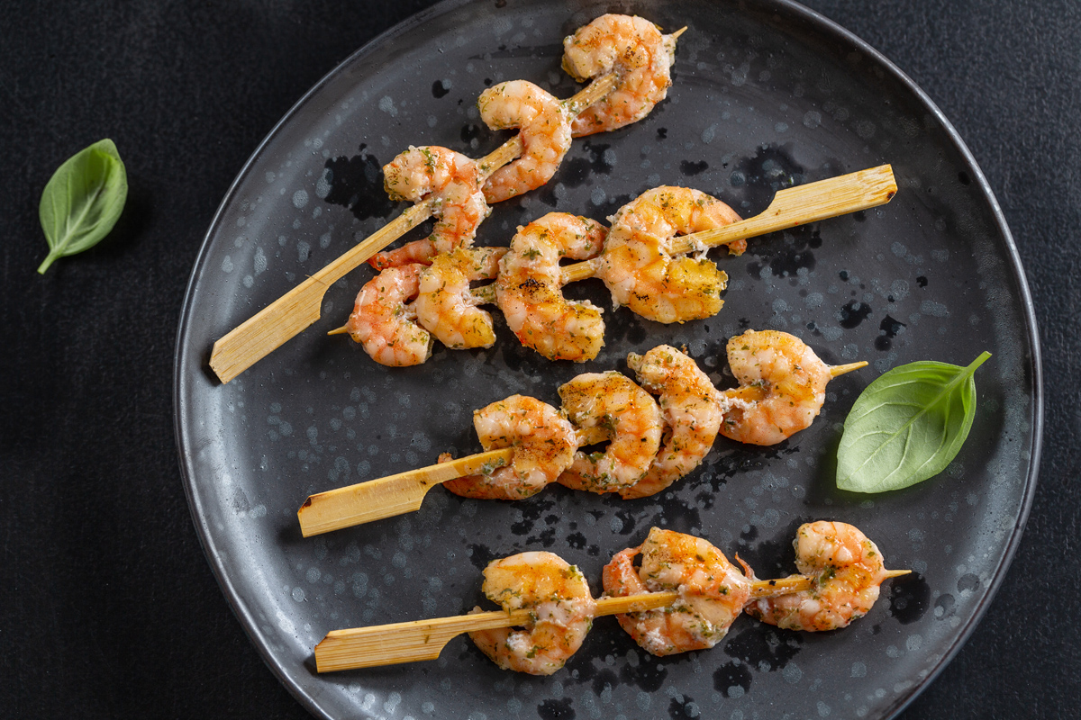 Shrimps On Skewer With Spices And Herbs Served On Dark Plate. Closeup.
